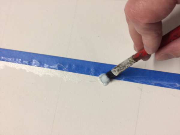 painting a sealant on the edge of a piece of tape on a canvas